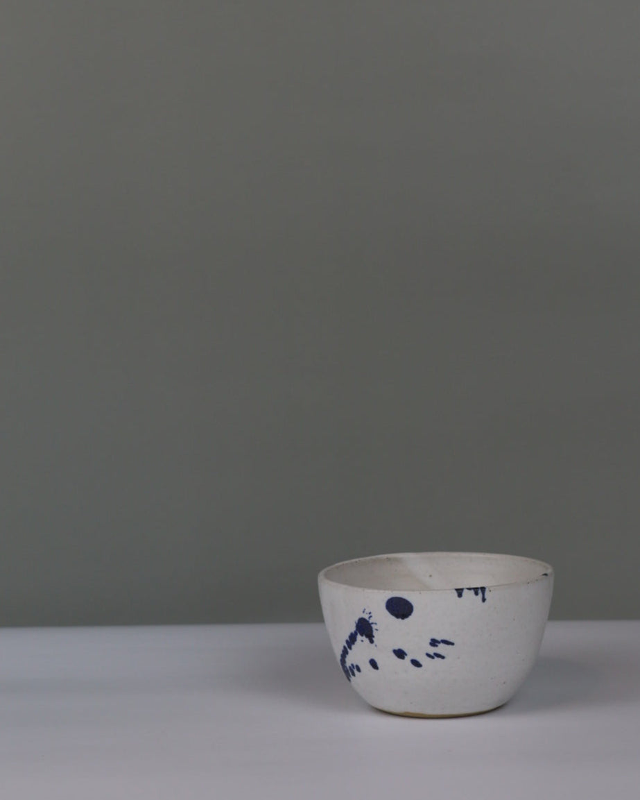 small ceramic bowl in white with blue splatter on a grey background