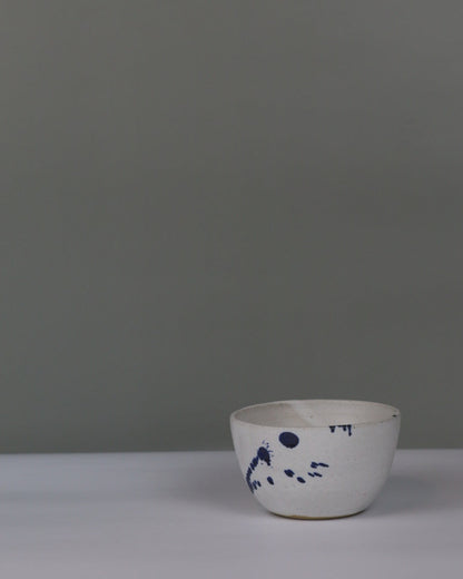 small ceramic bowl in white with blue splatter on a grey background