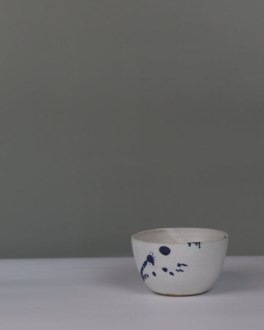 small ceramic bowl in white with blue splatter on a grey background
