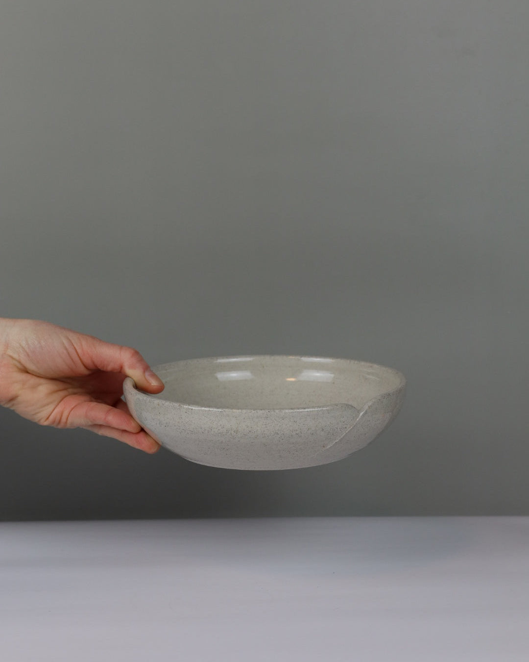 Hand holding a ceramic bowl against a plain background