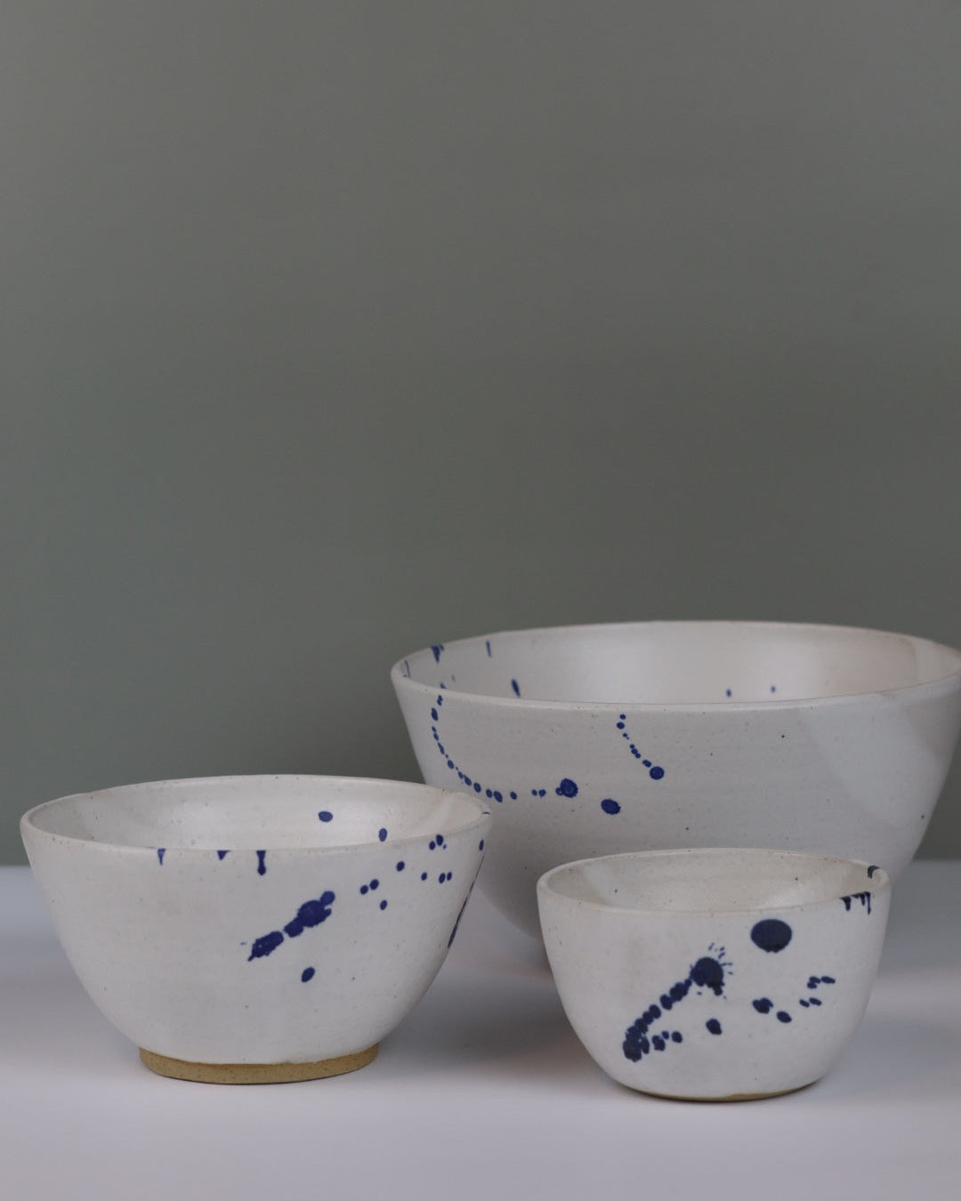 three ceramic bowls of different sizes in white with blue splatter on a grey background