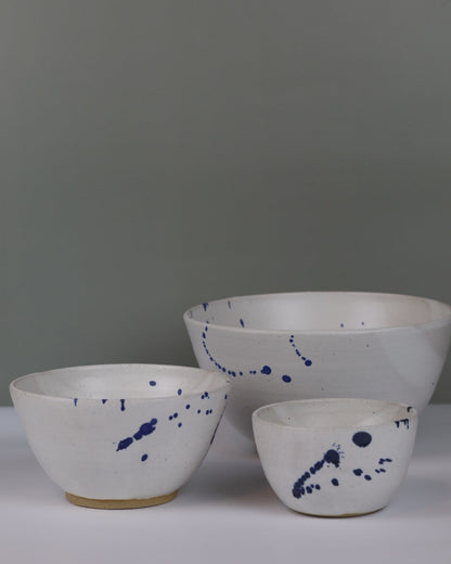 three ceramic bowls of different sizes in white with blue splatter on a grey background