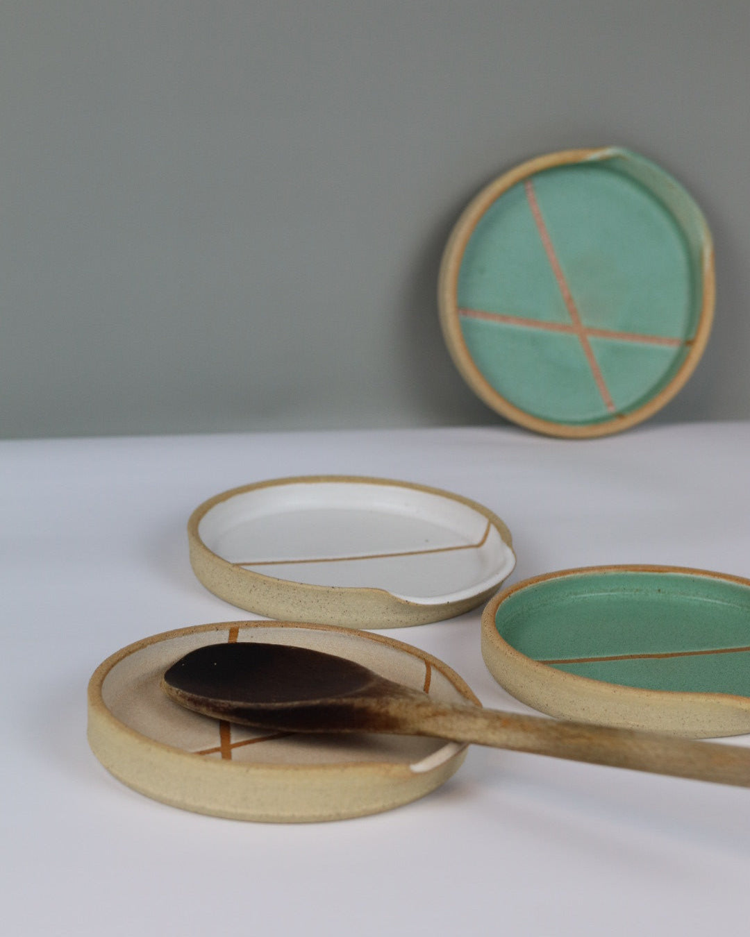 set of ceramic spoon rests with a wooden spoon on a benchtop